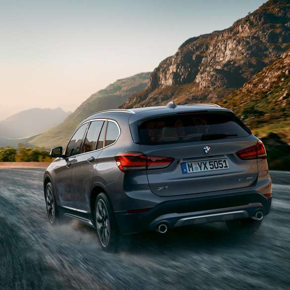 BMW X1, three-quarter rear view. BMW X1, three-quarter rear view driving in front of mountain scenery.