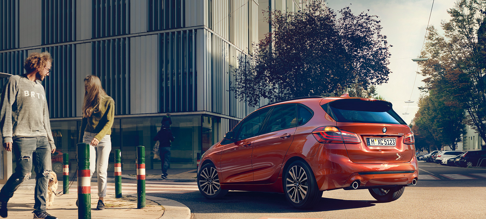 Three-quarter rear view BMW 2 Series Active Tourer 220i BMW 2 Series Active Tourer 220i F45 Sunset Orange metallic three-quarter rear view driving on the road