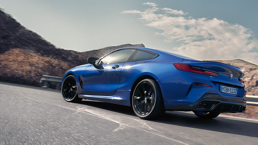 BMW 8 Series Coupé M Portimao Blue metallic G15 LCI Facelift three-quarter rear view driving in front of hills