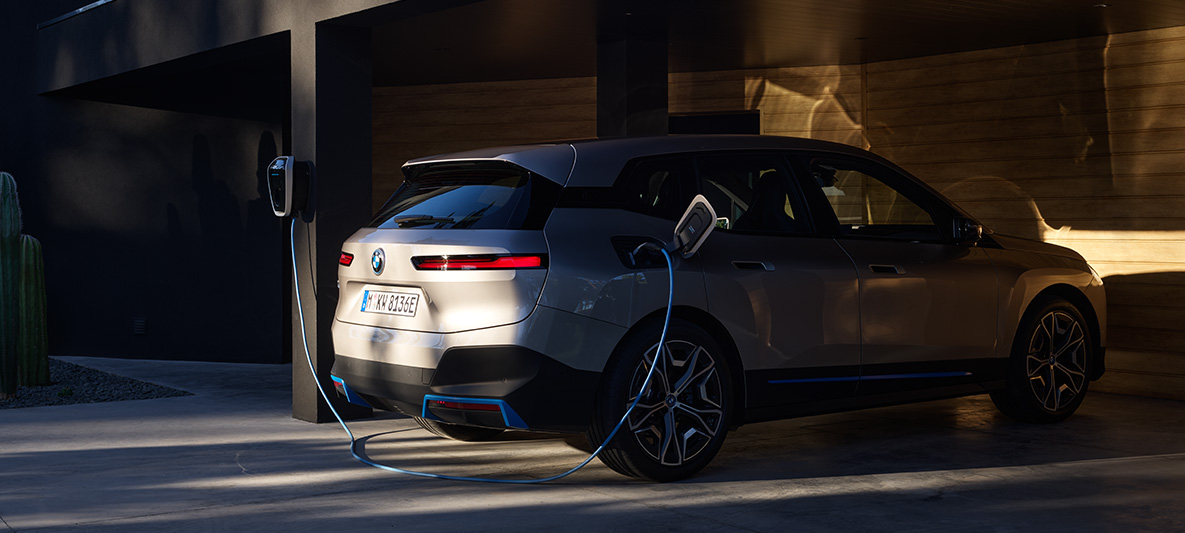 BMW iX three-quarter rear view charging on BMW Wallbox BMW iX Cashmere Silver i20 three-quarter rear view charging on BMW Wallbox