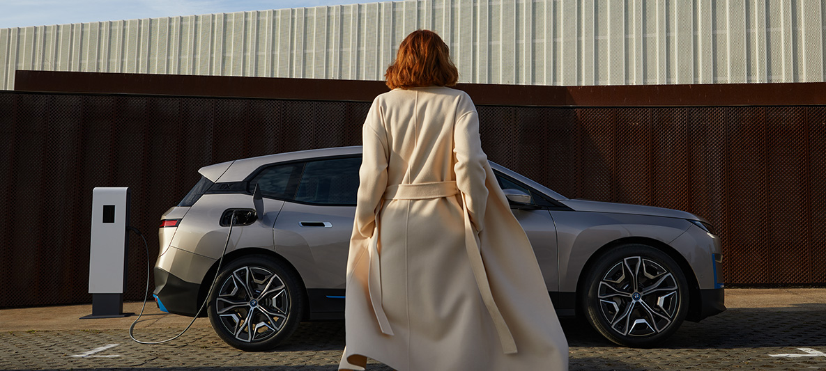BMW iX side view standing BMW iX Cashmere Silver i20 side view standing with model in front