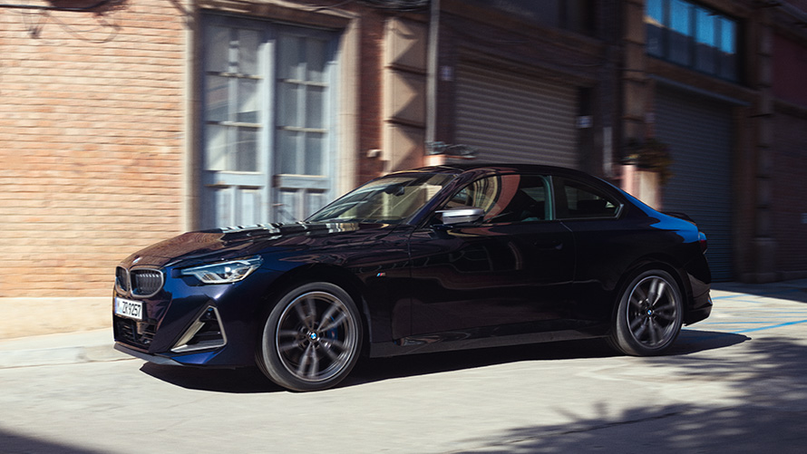 Three-quarter side view BMW M240i xDrive Coupé G42 2021 BMW 2 Series Coupé G42 2021 Thundernight metallic three-quarter side view standing in front of warehouse