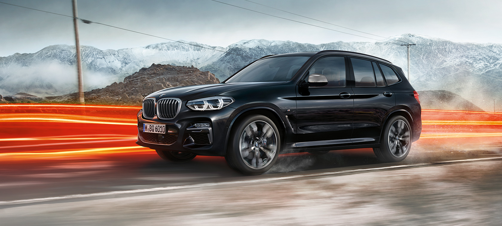 BMW X3 M40i side view. BMW X3 M40i in Black Sapphire metallic, driving, exterior, side view in front of mountain scenery with light strips.