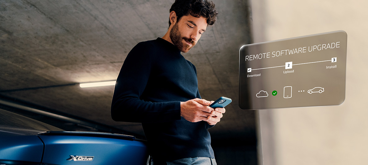 Man leaning against BMW rear and looking at his smartphone Remote Software Upgrade Man leaning against BMW rear and looking at his smartphone